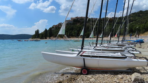 Sailboats moored on sea shore against sky