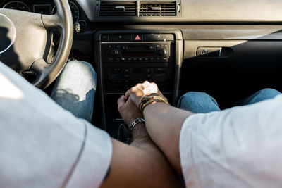 Back view of crop anonymous romantic couple in casual wear holding hands in car during road trip in sunny summer day