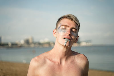 Shirtless man with glitter in mouth and face standing on beach