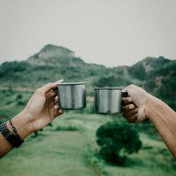 Cropped image of hand holding drink against sky