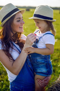 Daughter with mom standing in the field at the sheaf in hats and denim jumpsuits during sunset