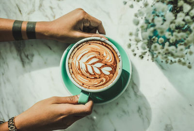 Cropped hands of man holding coffee cup on table