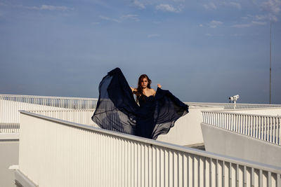 Woman sitting on railing against sky