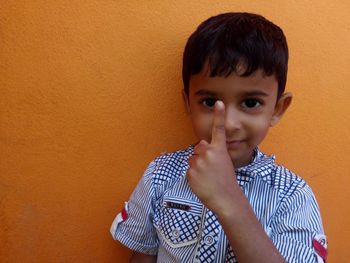 Portrait of boy showing finger while standing against orange wall