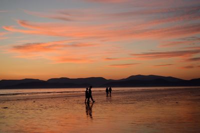 Silhouette people on beach against sky during sunset