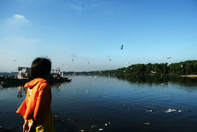 Girl standing by river against blue sky