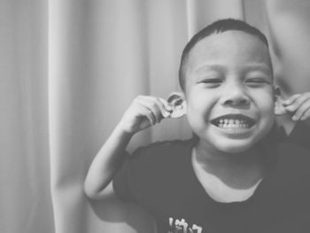 Close-up of cute boy pulling ears against curtain at home