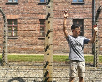 Boy standing by fence against brick wall