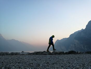 Man walking on rocks against sky during sunset