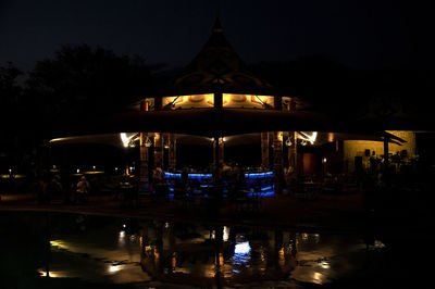 Illuminated building by lake against sky at night