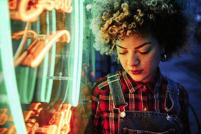 Curly haired woman looking down while standing by neon lights