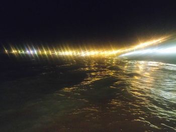 Illuminated street by sea against sky at night