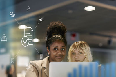 Smiling female colleagues in office, document computer icon in foreground