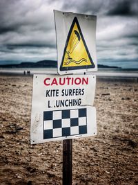 Close-up of information sign on beach against sky