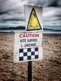 Close-up of warning sign at beach against sky