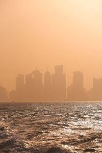 Sea by buildings against sky during sunset