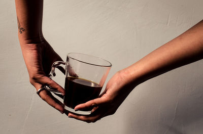 Cropped hands of woman holding coffee against wall