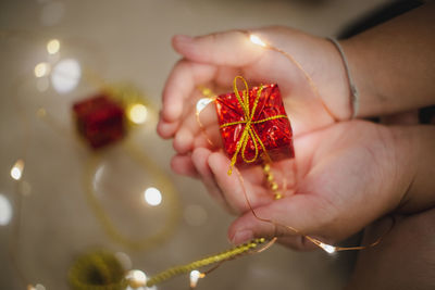 Cropped hands of person holding christmas present with illuminated fairy lights at home