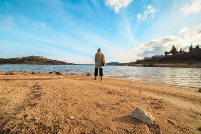 Rear view of woman standing on beach against sky