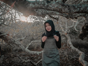 Portrait of young woman standing against trees