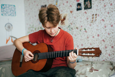 A teenage girl plays the acoustic guitar while sitting in her room.