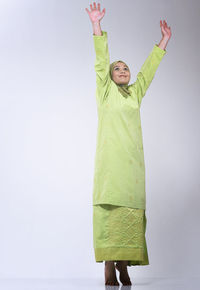 Woman in green hijab standing with arms raised against white background