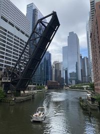 Boats in river amidst buildings in city against sky
