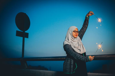 Woman with burning sparklers against blue sky at dusk