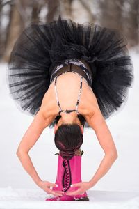 Dancer in black tutu and pink boots standing bent over in snow