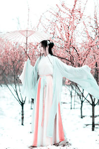 Young woman under umbrella standing against cherry tree