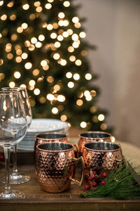 Close-up of holiday drinks on table illuminated by a christmas tree 