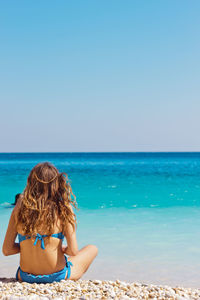 Rear view of woman on beach against clear blue sky
