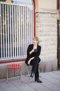 Full length of smiling mid adult businesswoman having coffee while sitting outside office