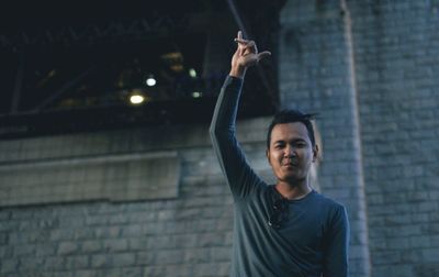 Portrait of man gesturing while standing against wall