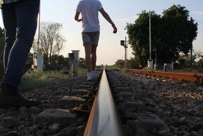 Low section of men walking on railroad track against sky