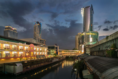 Illuminated buildings by river against sky at night