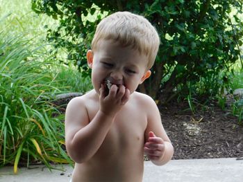 Close-up of shirtless baby boy eating food while standing at yard