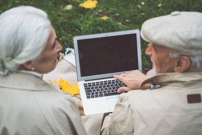 Rear view of couple video calling on laptop at park