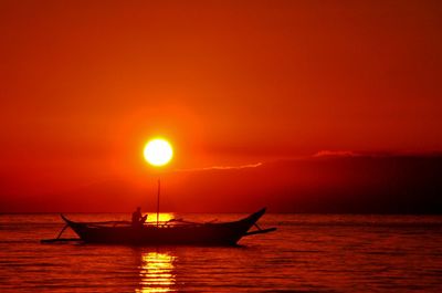 Silhouette boat in sea against orange sky