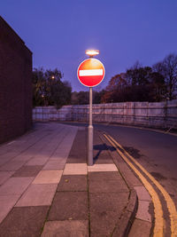 Illuminated road sign on footpath by street against sky