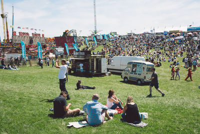 People relaxing on field against sky