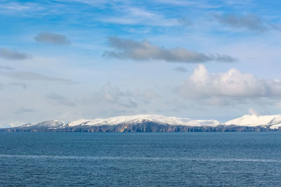 Scenic view of sea by snowcapped mountain against sky