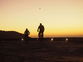 Silhouette man riding bicycle against sky during sunset