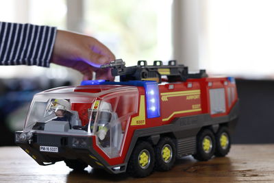 Cropped hand of child playing with toy fire engine at table