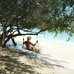 Shirtless man swinging at beach