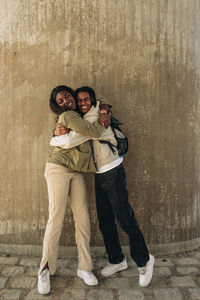 Happy male and female friend embracing each other while standing against wall