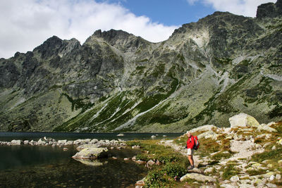 Side view of woman standing at lakeshore against mountains