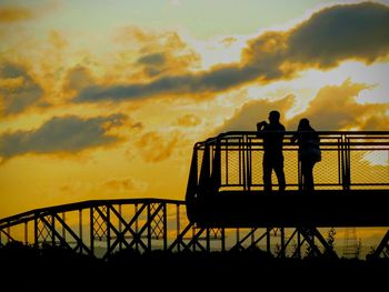 Silhouette men standing by railing against sky during sunset