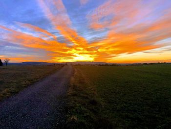 Road amidst field against sky during sunset