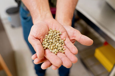 From above of crop unrecognizable farmer demonstrating heaps of fresh raw coffee beans in palms on blurred background